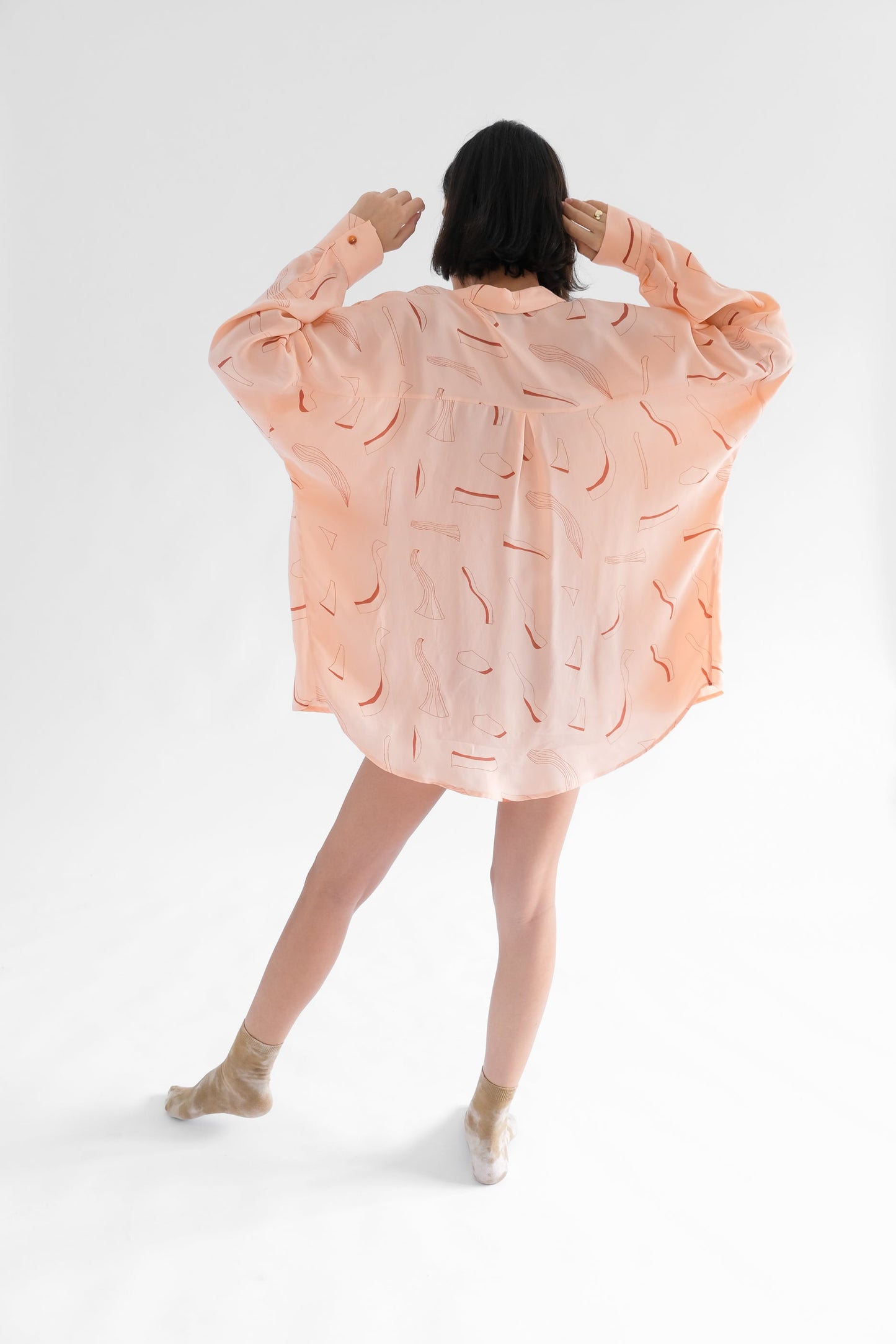 Girl standing backwards wearing pink silk printed shirt